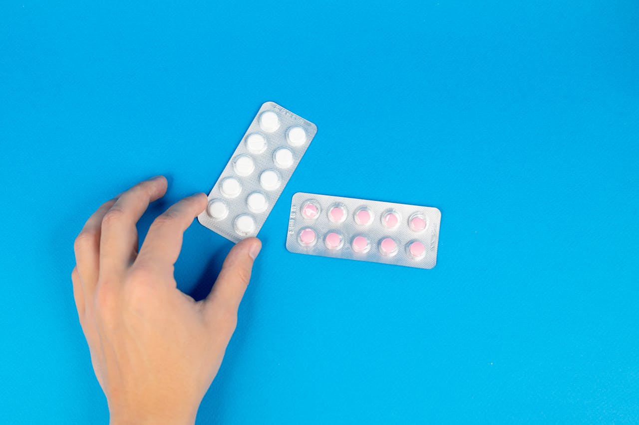 Image of a hand reaching for blister packs against a blue background, offering copy space.